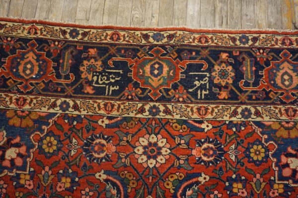 A detailed traditional rug in red, navy, and cream with dense floral motifs resting on wood planks.