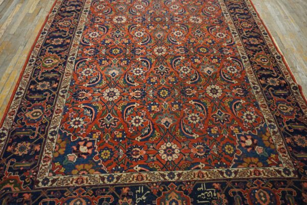 Ornate floral rug with a rust-red field and navy blue border on rustic wooden floor.