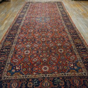 Intricate red and navy floral runner rug with a dark border displayed on distressed wood flooring.