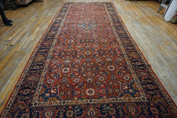 Intricate red and navy floral runner rug with a dark border displayed on distressed wood flooring.