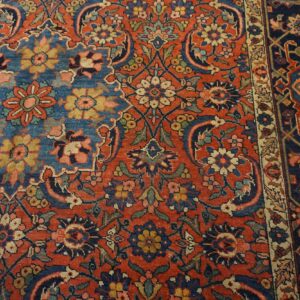 Densely patterned rug detail featuring a red field with intricate floral motifs and a contrasting dark blue border.