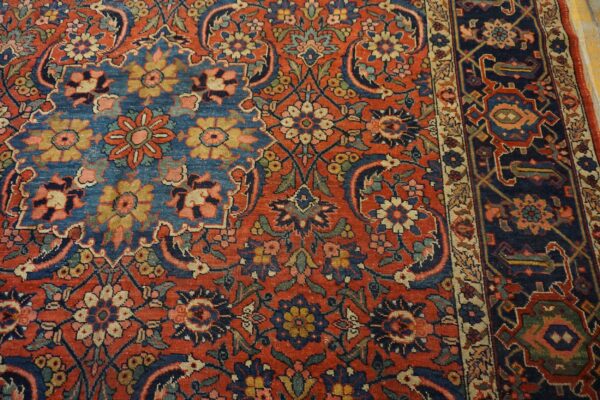Densely patterned rug detail featuring a red field with intricate floral motifs and a contrasting dark blue border.