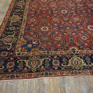 Intricate red rug featuring a dark blue border and multicolored floral motifs covers rustic wood planks.
