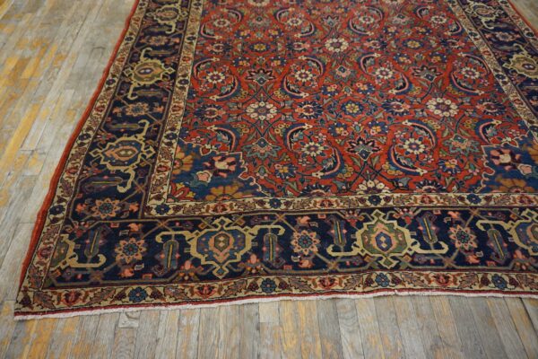 Intricate red rug featuring a dark blue border and multicolored floral motifs covers rustic wood planks.