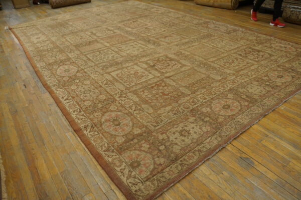 Large faded rug with repeating beige and rust floral motifs covers a distressed wood floor.