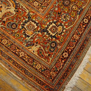 Intricate red, navy, and cream floral rug pattern with visible fringe on rustic amber wood planks.