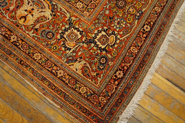 Intricate red, navy, and cream floral rug pattern with visible fringe on rustic amber wood planks.