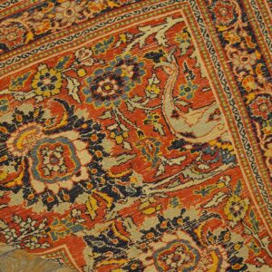A detailed view of an intricate red, navy, and cream patterned rug folded onto light wood plank flooring.