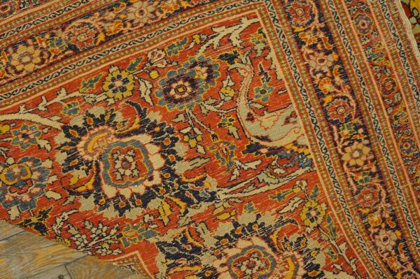 A detailed view of an intricate red, navy, and cream patterned rug folded onto light wood plank flooring.