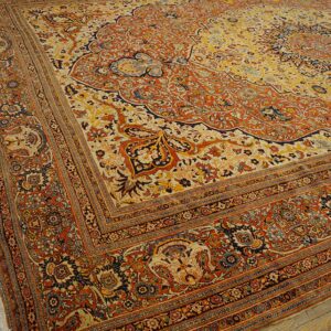 Intricate traditional rug featuring a detailed floral medallion in orange, yellow, and navy on wood planks.