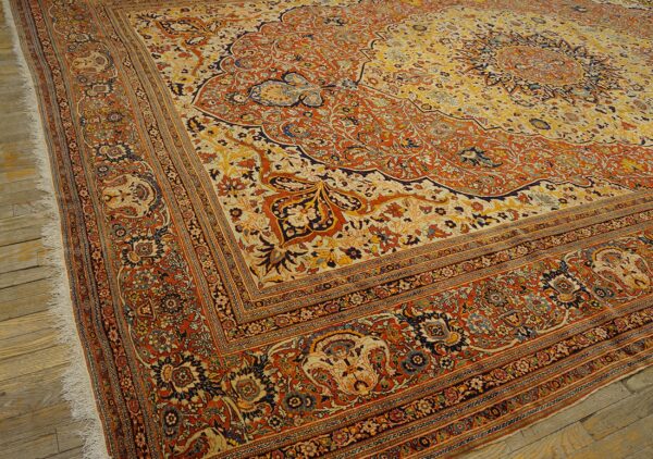 Intricate traditional rug featuring a detailed floral medallion in orange, yellow, and navy on wood planks.