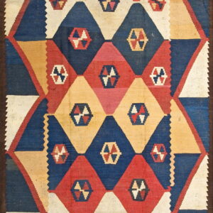 Flatwoven rug featuring large interlocking diamond patterns in blue, red, yellow, and cream colors with a dark border.