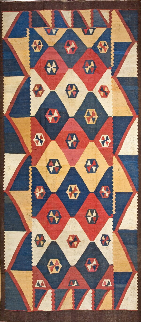 Flatwoven rug featuring large interlocking diamond patterns in blue, red, yellow, and cream colors with a dark border.