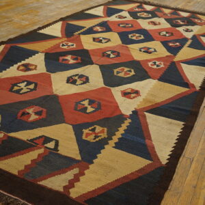 Flatweave rug with a geometric pattern of navy, tan, and red diamonds on rustic wood flooring.