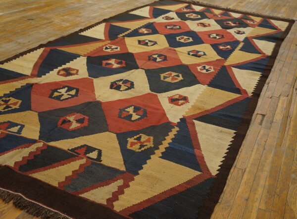 Flatweave rug with a geometric pattern of navy, tan, and red diamonds on rustic wood flooring.
