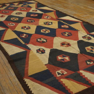 Geometric flatweave runner rug in navy, red, cream, and gold on rustic wooden plank flooring.