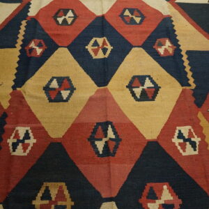 Geometric flatweave rug with navy, red, and tan diamonds on light brown hardwood flooring.