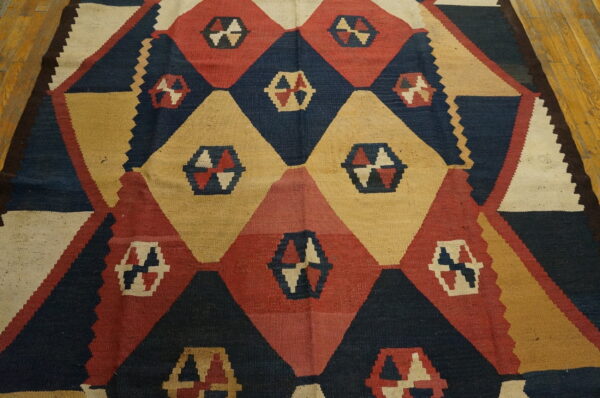 Geometric flatweave rug with navy, red, and tan diamonds on light brown hardwood flooring.