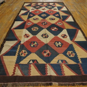 Long, flat-woven rug with red, navy, and cream geometric diamond patterns on wood flooring.
