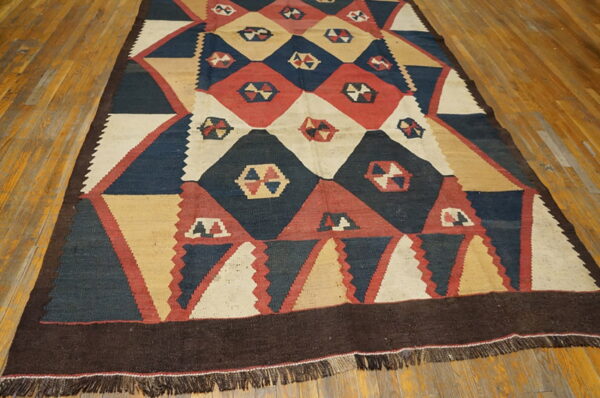 Geometric flatweave rug featuring diamonds and triangles in navy, red, tan, and cream on a wooden floor.