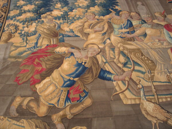 A pictorial flat-woven textile shows classical figures, including one kneeling with a bow, in gold, blue, and red.