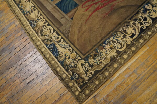 Muted brown and gold rug with an ornate scroll border on distressed wooden plank flooring.