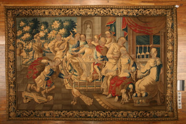 A large tapestry rug featuring a classical banquet scene in beige, blue, green, and red tones.
