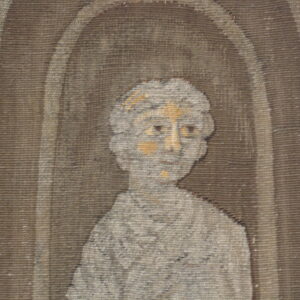 Woven rug detail showing a gray and tan stylized bust within a dark brown arched niche.