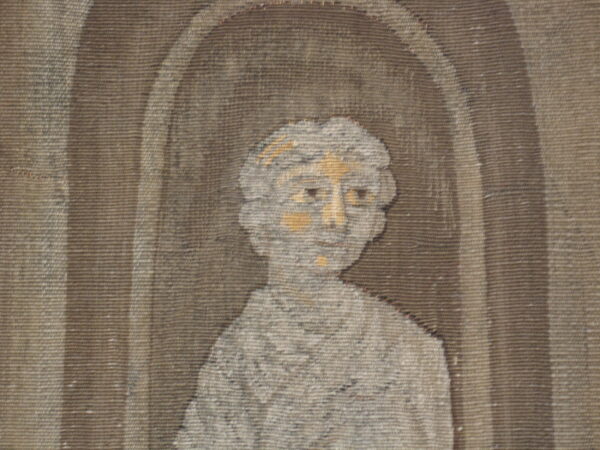 Woven rug detail showing a gray and tan stylized bust within a dark brown arched niche.