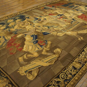 Large, low-pile rug displays a figural narrative pattern in gold, navy, and brown on distressed wood planks.