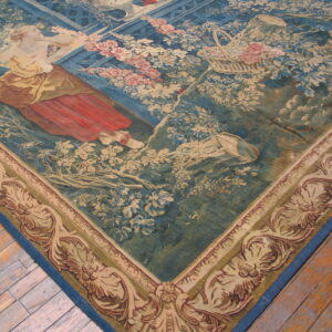 Blue tapestry rug depicting a woman in red and a floral garden, visible on wood planks.