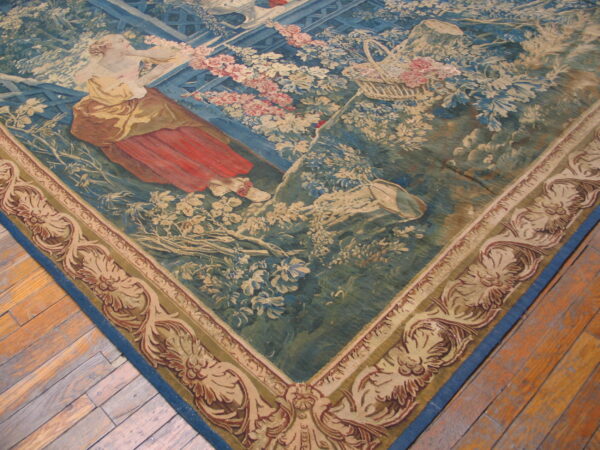 Blue tapestry rug depicting a woman in red and a floral garden, visible on wood planks.