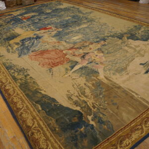 Large tapestry rug depicting classical figures in muted blue, tan, and red on worn wood flooring.
