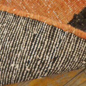 The curled runner rug edge reveals a striped woven backing and thick orange binding on wood floors.