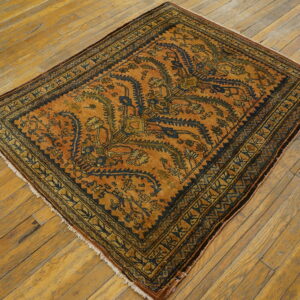 Rust-colored rug with intricate dark blue and green patterns displayed on worn wooden floorboards.