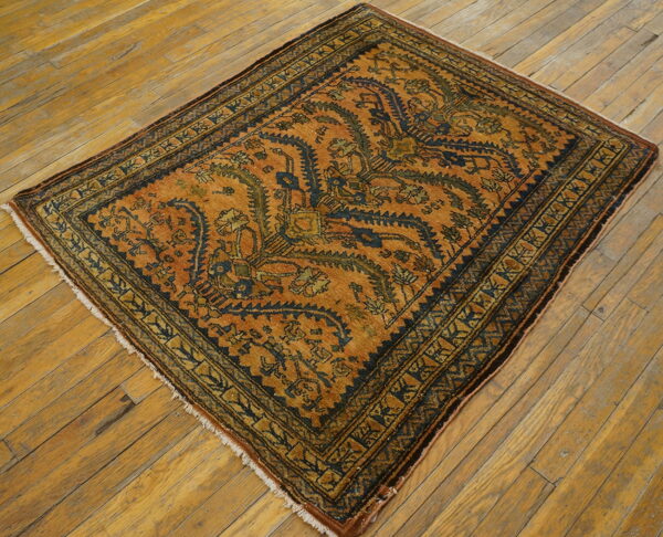 Rust-colored rug with intricate dark blue and green patterns displayed on worn wooden floorboards.