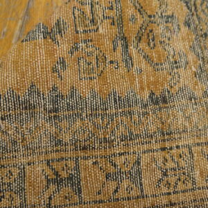 Flatweave rug in amber and navy geometric patterns, folded slightly on worn wood planks.