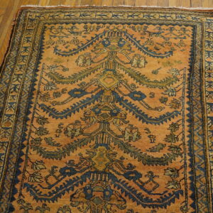 Saffron-orange rug featuring a dark blue stylized tree design and detailed borders on hardwood flooring.