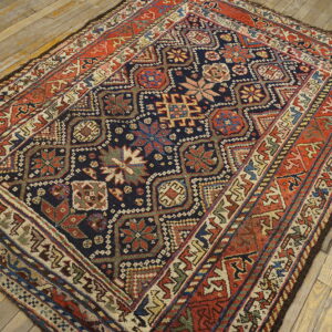 Geometric rug featuring a navy and red medallion pattern, laid on distressed light wood plank flooring.