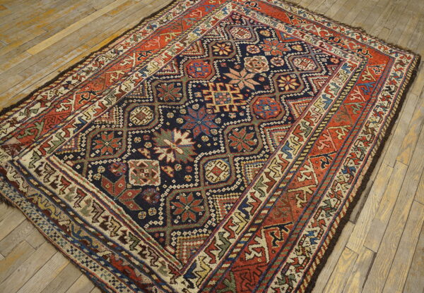 Geometric rug featuring a navy and red medallion pattern, laid on distressed light wood plank flooring.