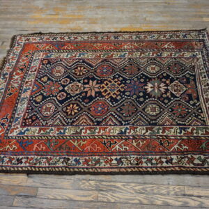 Traditional geometric rug in navy and rust red with multicolored motifs on distressed wood floors.