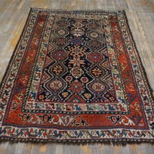 Low-pile rug with a detailed navy field and red geometric border rests on gray-washed hardwood flooring.