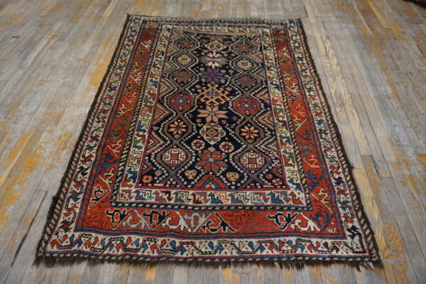 Low-pile rug with a detailed navy field and red geometric border rests on gray-washed hardwood flooring.