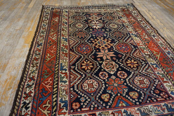 Low pile rug with complex geometric patterns in navy, red, and beige on weathered wood planks.