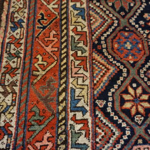 Detailed view of a tribal rug pattern in navy, red, and beige on distressed wood flooring.