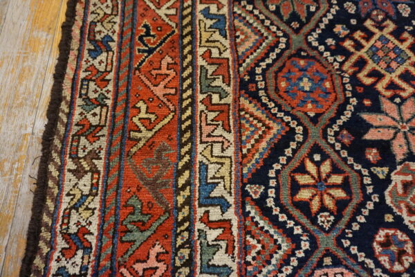 Detailed view of a tribal rug pattern in navy, red, and beige on distressed wood flooring.