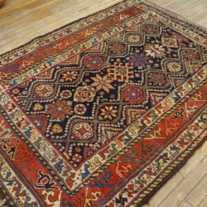 Dark navy and rust geometric area rug on light wood plank flooring, with an orange utility object nearby.
