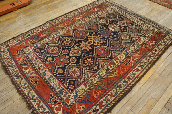 Dark navy and rust geometric area rug on light wood plank flooring, with an orange utility object nearby.