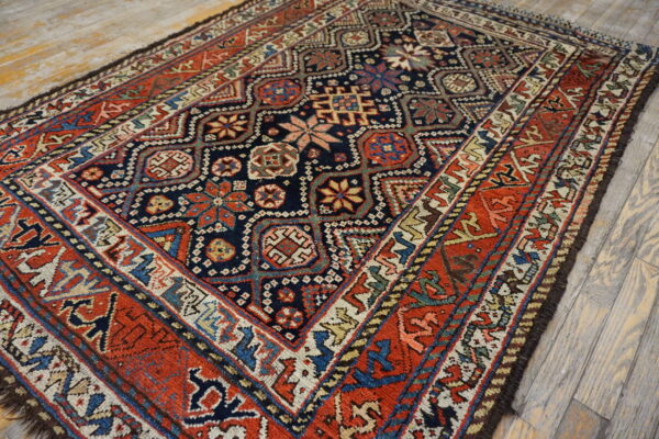 Navy blue and terracotta rug with complex geometric motifs rests on distressed light wood plank flooring.