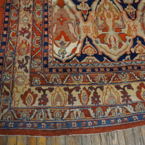 Ornate traditional rug in navy, rust red, and beige lying on distressed wooden floors.
